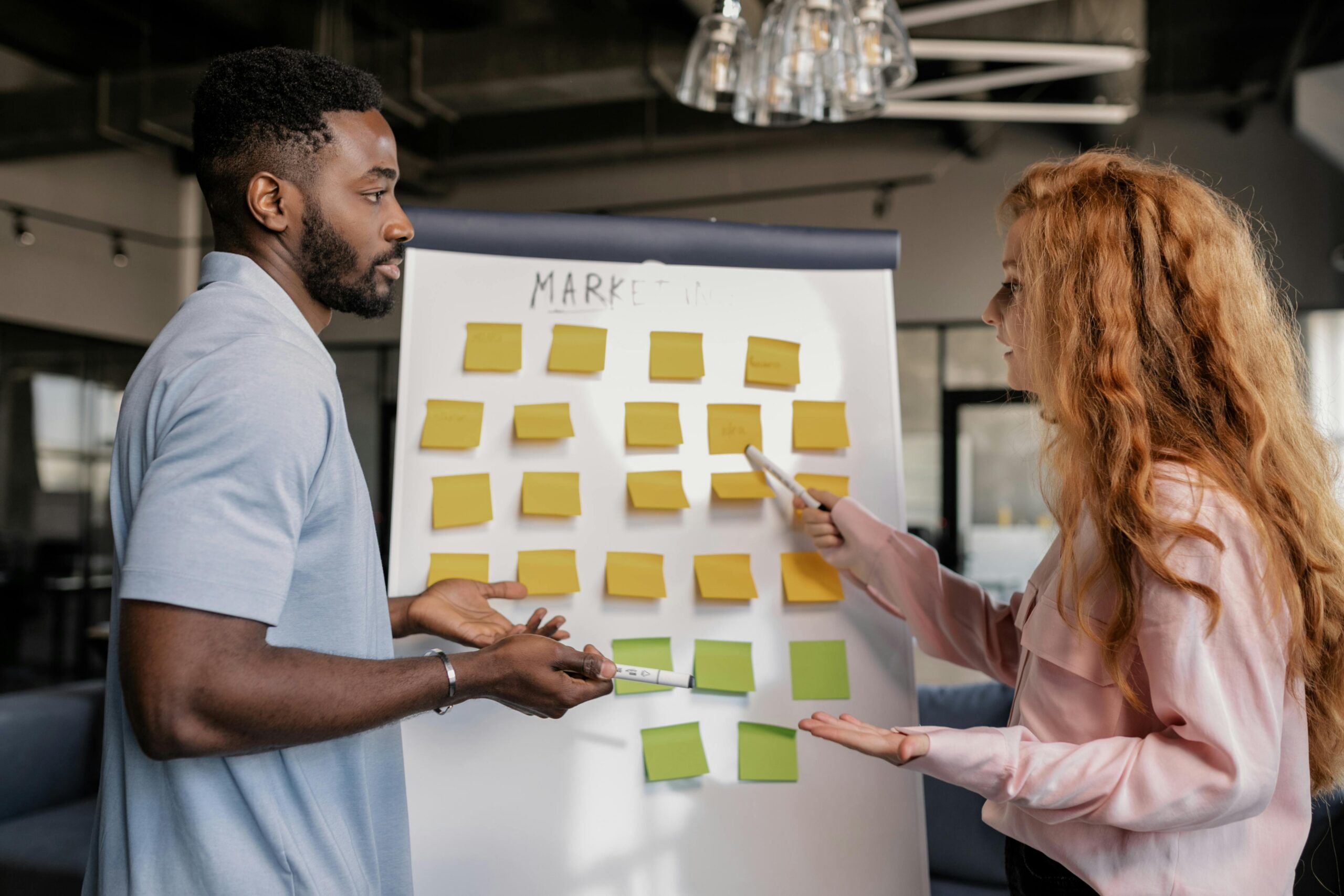 A man and woman discuss at a whiteboard populated with sticky notes.