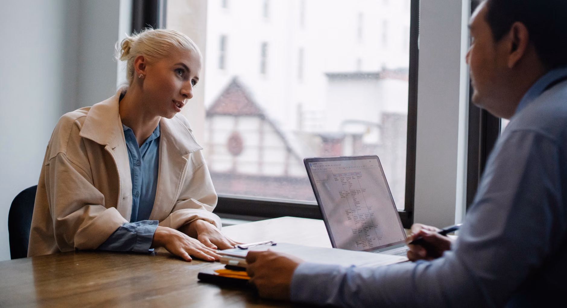 A professional leans over a conference room table in serious discussion with a colleague